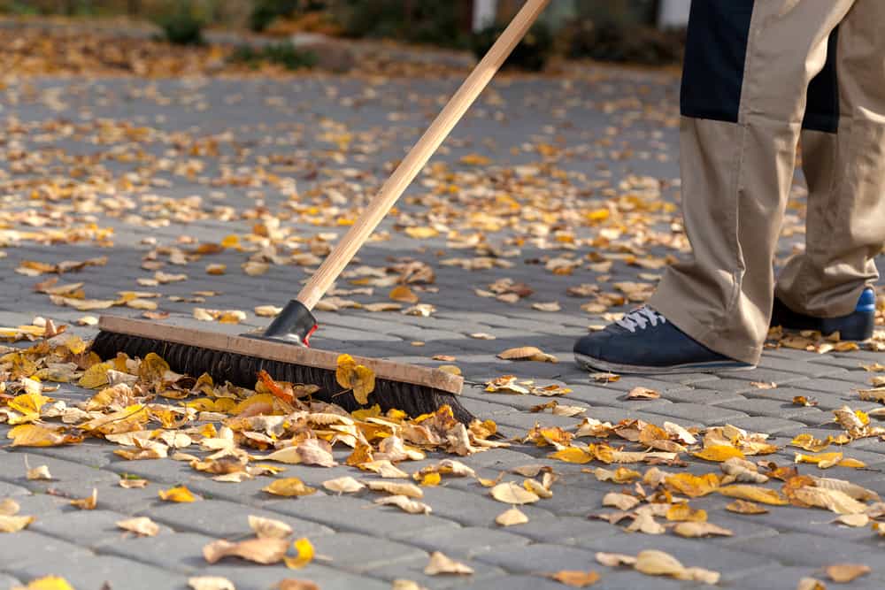 Worker cleaning up the driveway from autumn leaves Worker cleaning up the driveway from autumn leaves